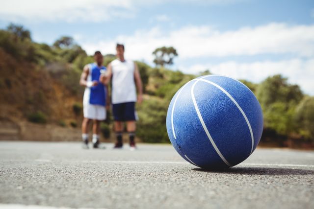 Blue basketball on ground with player standing in background - Download Free Stock Photos Pikwizard.com