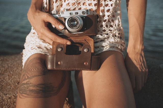 A female photographer with a tattoo holds a film camera on her lap - Design elements with a classic look are making a comeback - Image