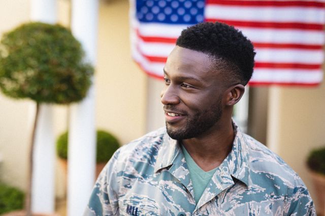 Smiling african american mid adult male soldier looking away with us flag in background. unaltered, us military, happiness and homecoming.