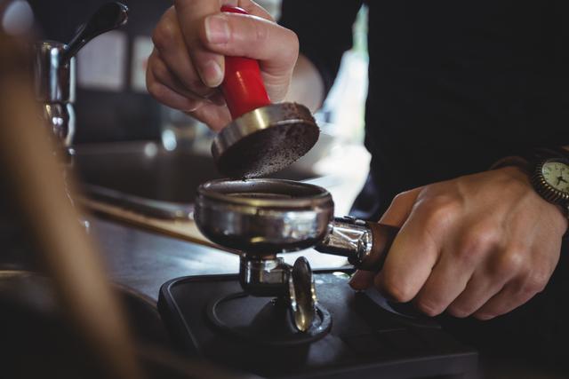 Close-up of waitress using a tamper to press ground coffee into a portafilter in cafe