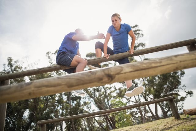 Man assisting woman to climb a hurdles during obstacle training - Download Free Stock Photos Pikwizard.com