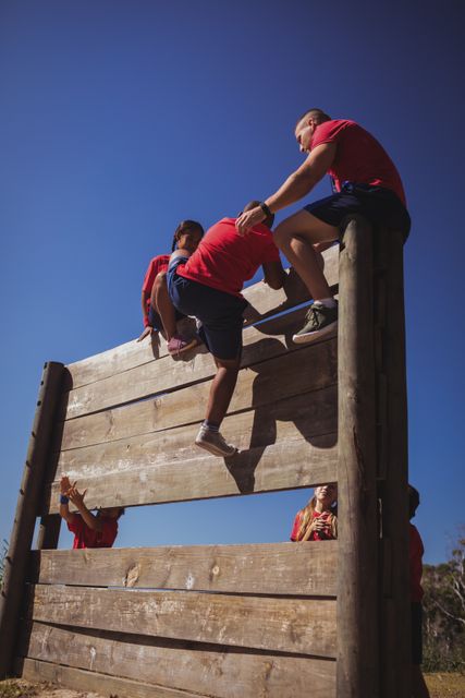 Trainer assisting kids to climb a wooden wall during obstacle course training - Download Free Stock Photos Pikwizard.com