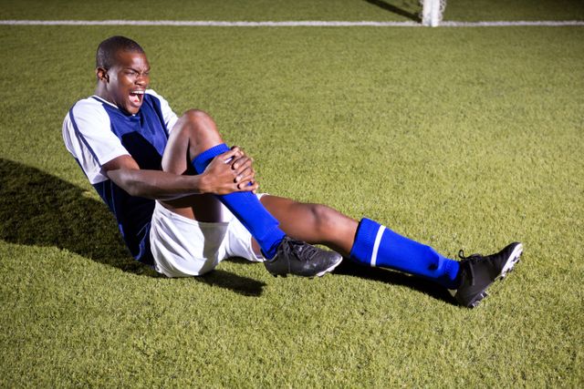 Young male soccer player shouting in agony with knee pain on playing field