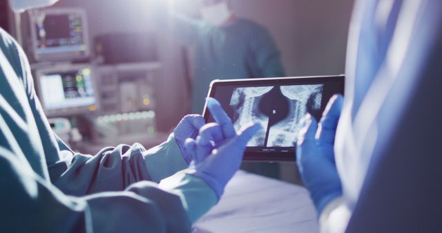Image of midsection of two gloved surgeons discussing x-ray on tablet in operating theatre - Download Free Stock Photos Pikwizard.com