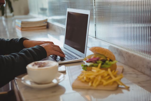 Cropped hands of man using laptop by coffee cup and French fries - Download Free Stock Photos Pikwizard.com