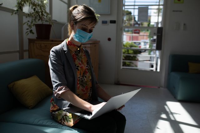 A caucasian woman sitting on the couch at an office wearing a facemask - Download Free Stock Photos Pikwizard.com