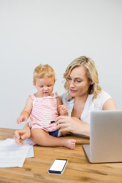 Mother holding baby girl while writing notes on paper - Download Free Stock Photos Pikwizard.com