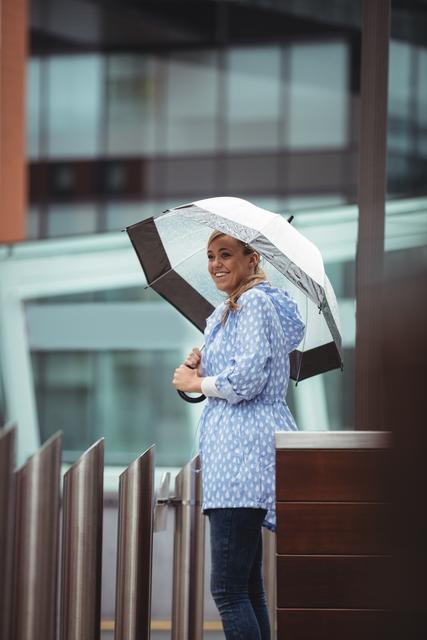 Beautiful woman holding umbrella and standing on street during rainy season