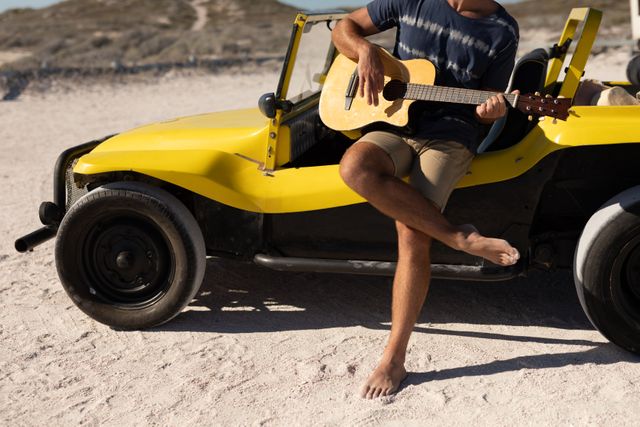 Low section of caucasian man sitting on beach buggy playing guitar on sunny beach - Download Free Stock Photos Pikwizard.com