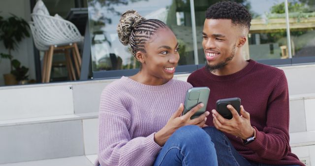 Happy african american couple talking and relaxing with smartphones outside house. Lifestyle, relationship, spending free time together concept.