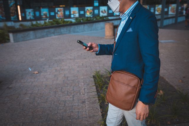 Mid section of asian man wearing face mask using smartphone while walking at at corporate park - Download Free Stock Photos Pikwizard.com