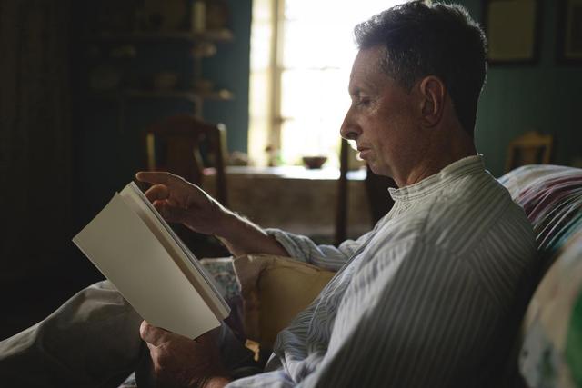Senior man reading a novel in living room - Download Free Stock Photos Pikwizard.com
