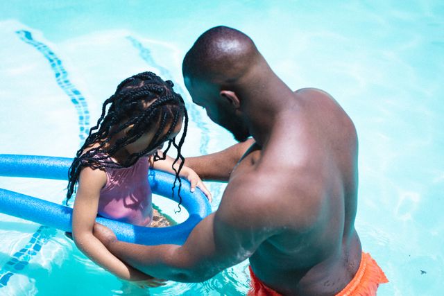 African american father helping daughter with swimming float in pool on sunny day - Download Free Stock Photos Pikwizard.com
