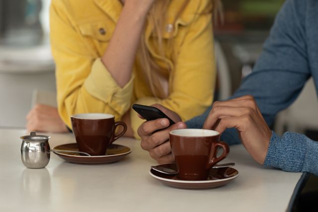 Mid section of couple using smartphone while having coffee - Download Free Stock Photos Pikwizard.com