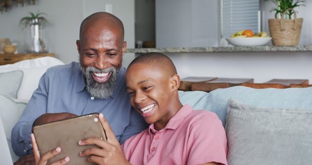 Image of happy african american father and son using tablet together. Family, spending quality time together at home.