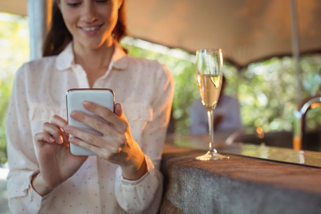 Smiling woman using mobile phone while having a glass of champagne - Download Free Stock Photos Pikwizard.com