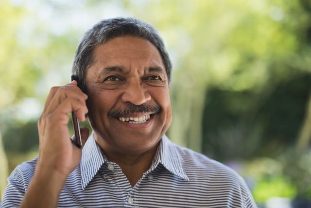 Smiling senior man looking away while talking on mobile phone at porch