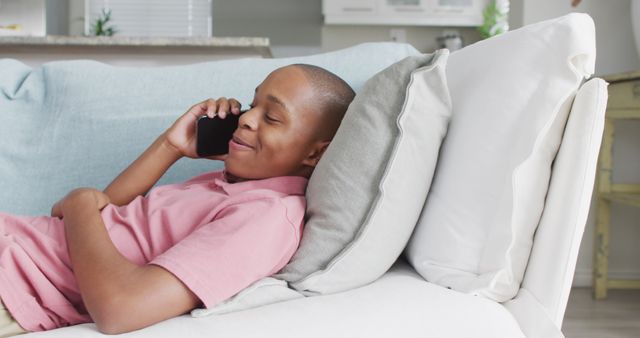 Image of happy african american boy using smartphone on sofa. Childhood, spending time with technology at home concept.