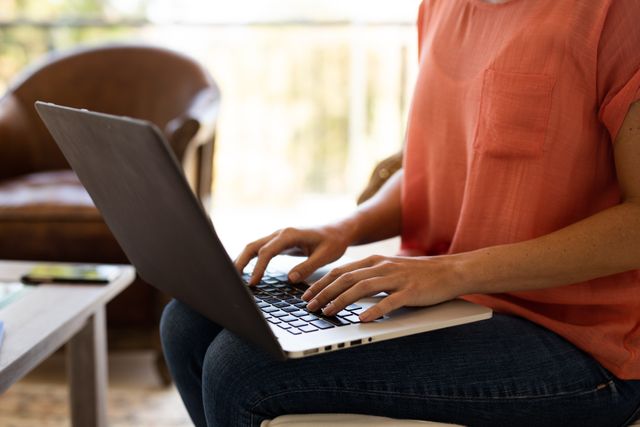 A caucasian woman sitting on a couch in their living room at home while typing on her laptop - Download Free Stock Photos Pikwizard.com
