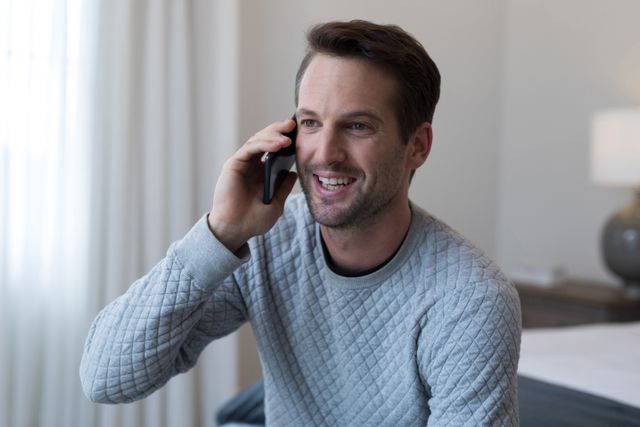 Happy man talking on mobile phone in bedroom