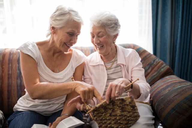 Cheerful senior women talking about knitting while sitting on sofa against window - Download Free Stock Photos Pikwizard.com