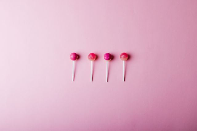 Overhead view of lollipops arranged side by side amidst copy space against pink background. unaltered, unhealthy eating and sweet food concept.