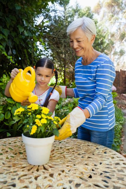 Smiling senior woman standing by granddaughter watering yellow flowers on table - Download Free Stock Photos Pikwizard.com