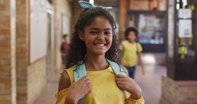 Portrait of happy mixed race schoolgirl standing in corridor looking at camera. children in primary school.