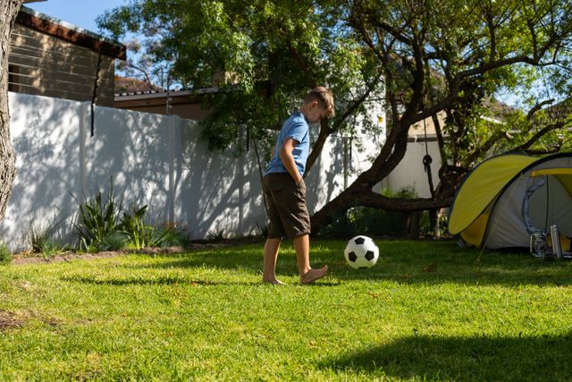 Caucasian boy kicking a ball around in their back yard - Download Free Stock Photos Pikwizard.com