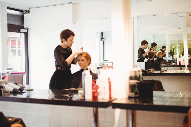 Female hairdresser styling clients hair in saloon