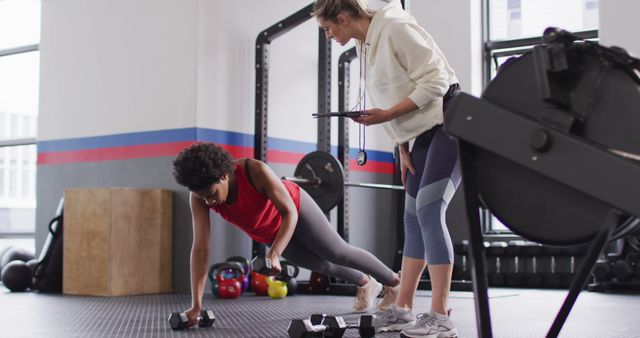 Image of diverse female fitness trainer instructing woman raising dumbbells working out at a gym - Download Free Stock Photos Pikwizard.com