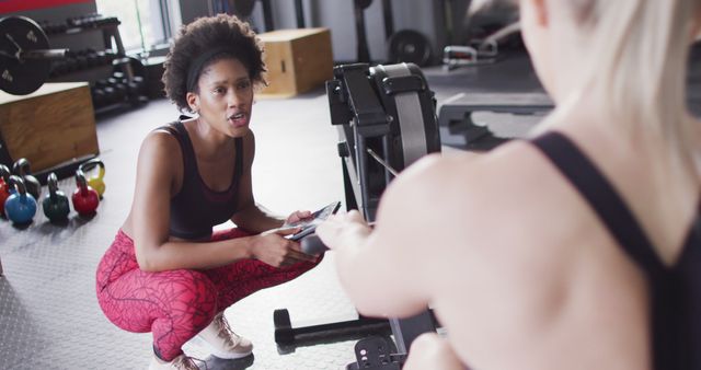Image of diverse, happy female trainer encouraging woman on rowing machine working out at a gym. Exercise, fitness and healthy lifestyle.