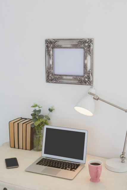 Electronic gadgets, lamp, book, mug, flora and book on table against white wall