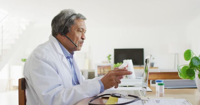 Senior biracial male doctor using headset and laptop for image consultation call. Medical services, communication, telemedicine, healthcare and inclusivity concept.