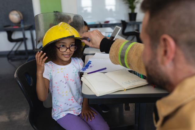 Firefighter wearing helmet to schoolgirl in classroom - Download Free Stock Photos Pikwizard.com
