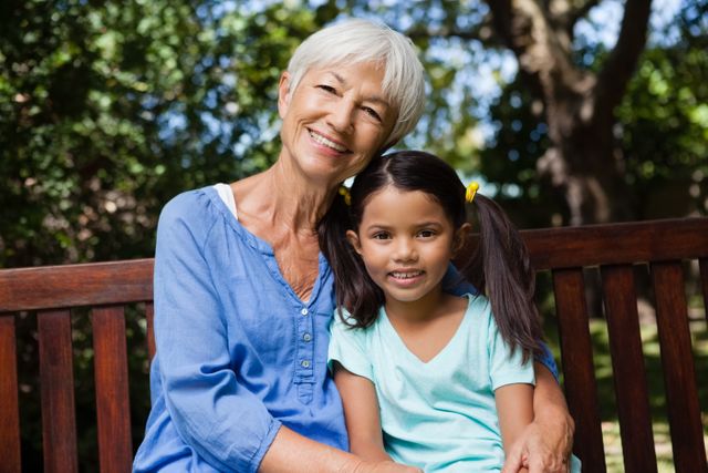 Portrait of smiling girl and grandmother sitting on wooden bench - Download Free Stock Photos Pikwizard.com