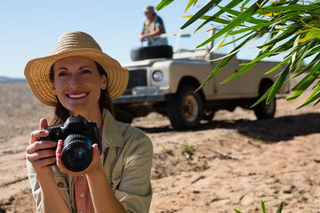 Smiling woman holding camera with man on off road vehicle at landscape