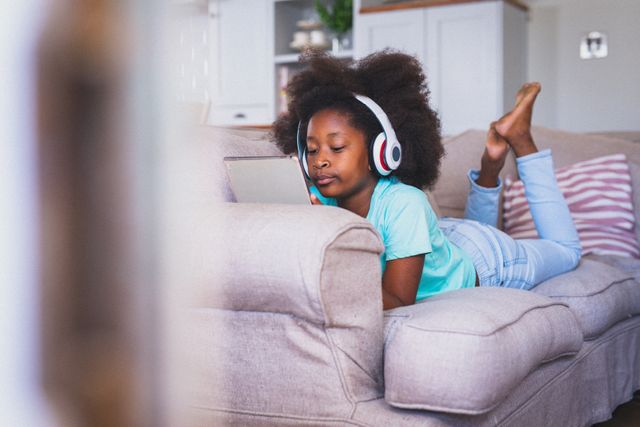 African american girl wearing headphones lying on couch using tablet - Download Free Stock Photos Pikwizard.com