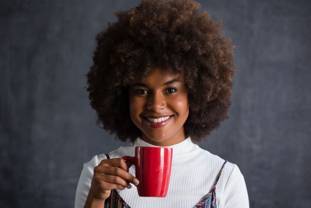 Smiling woman with frizzy hair holding coffee mug against wall - Download Free Stock Photos Pikwizard.com