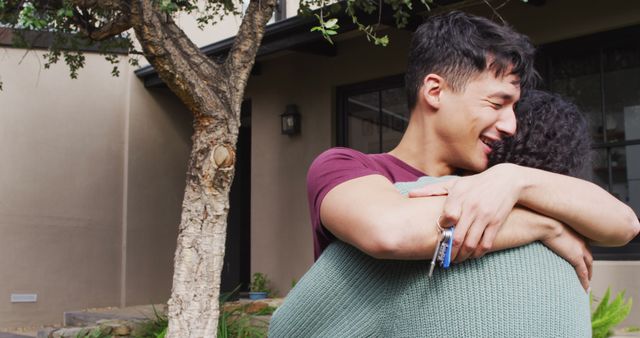 Happy diverse male moving house, holding keys, embracing and smiling. Spending quality time at home.