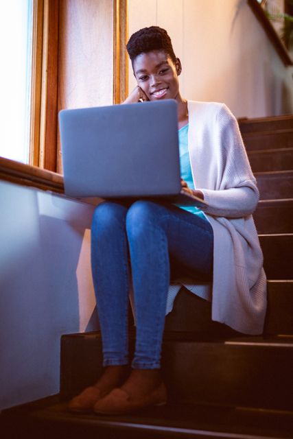 Happy african american woman sitting on stairs with laptop - Download Free Stock Photos Pikwizard.com