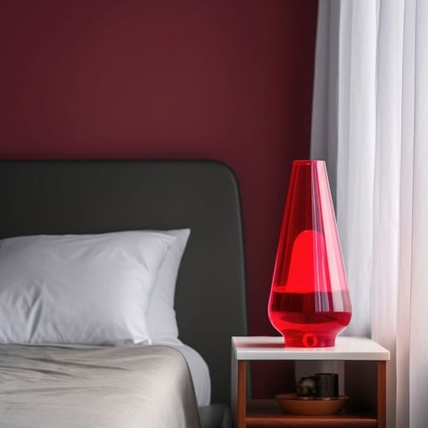 Red lava lamp on bedside table in bedroom in daylight, created using