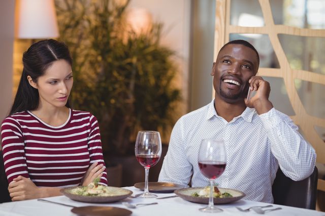 Man ignoring bored woman while talking on mobile phone in restaurant