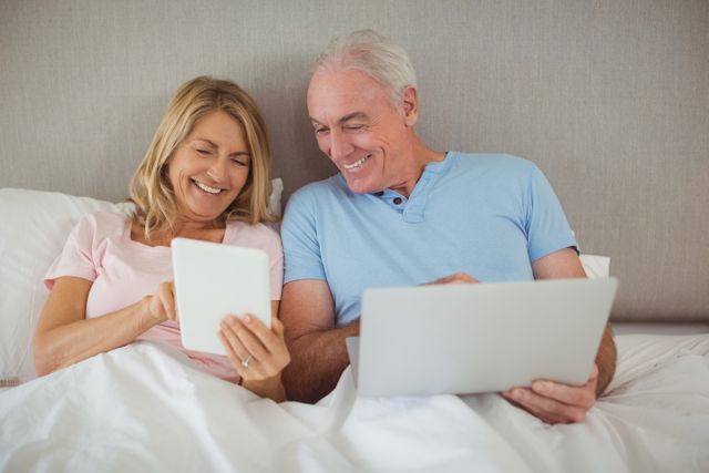 Happy senior couple on bed using laptop and digital tablet - Download Free Stock Photos Pikwizard.com