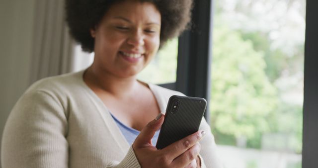 Image of happy plus size african american woman using smartphone. lifestyle, leisure, spending free time at home with technology.