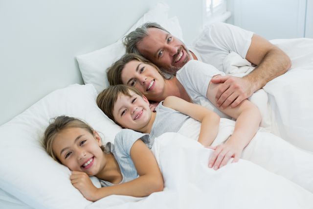 Happy family lying together on bed in bedroom at home - Download Free Stock Photos Pikwizard.com