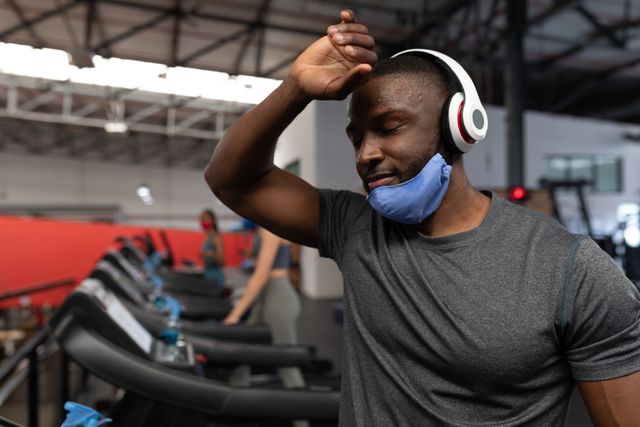 African american man in the gym wearing headphones wiping his sweat with his hand - Download Free Stock Photos Pikwizard.com