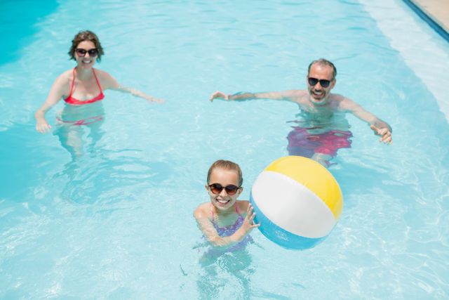 Happy parents and daughter playing with swim ball in swimming pool - Download Free Stock Photos Pikwizard.com