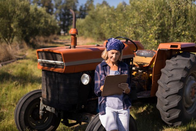 Woman leaning on tractor while writing on clipboard - Download Free Stock Photos Pikwizard.com