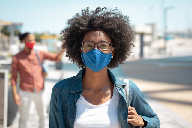 African american woman wearing face mask walking in sunny urban street - Download Free Stock Photos Pikwizard.com